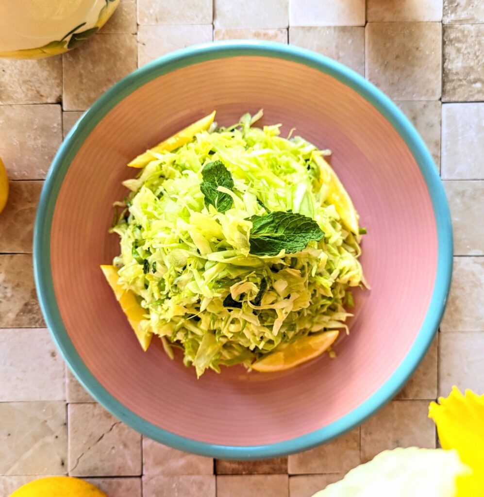 Vibrant cabbage salad with mint and fresh lemon, served on a pink plate with a turquoise rim.