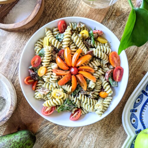 A colorful bowl of BLT rotini pasta salad tossed with avocado buttermilk ranch. Garnished with an orange, red, and yellow flowers made of small variety tomatoes.