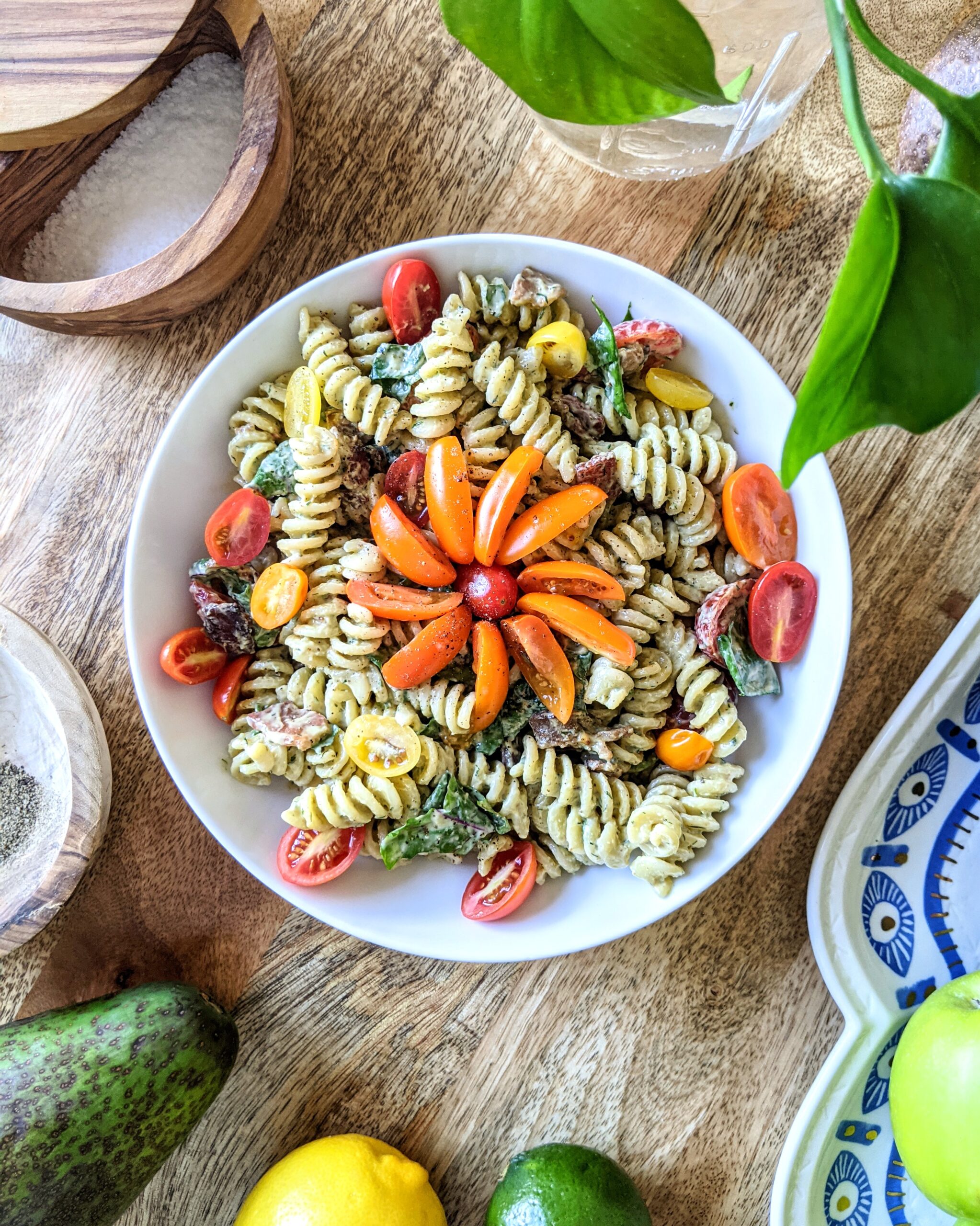 A colorful bowl of BLT rotini pasta salad tossed with avocado buttermilk ranch. Garnished with an orange, red, and yellow flowers made of small variety tomatoes.
