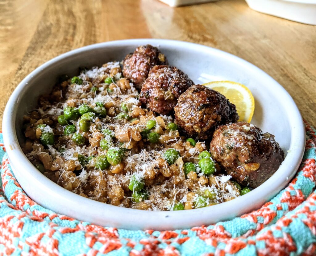 A side view of 4 baked meatballs, served with lemon and mint barley risotto.