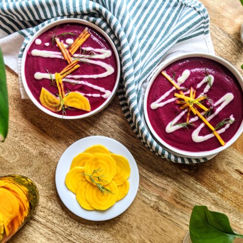 Two bowls of vibrant purple beetroot gazpacho; topped with a zigzag design of sour cream, julienned pickled golden beets, and fresh dill.