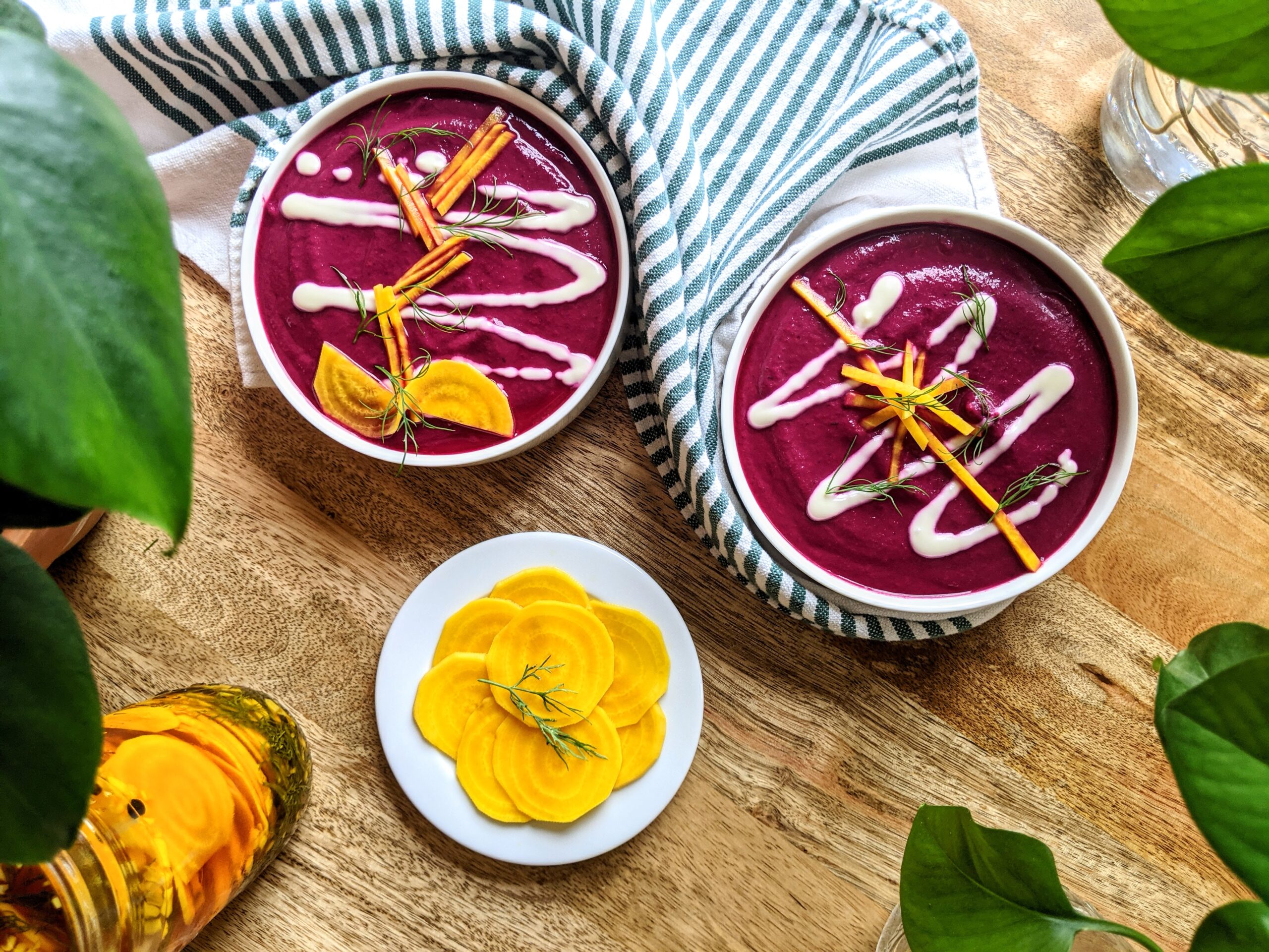Two bowls of vibrant purple beetroot gazpacho; topped with a zigzag design of sour cream, julienned pickled golden beets, and fresh dill.