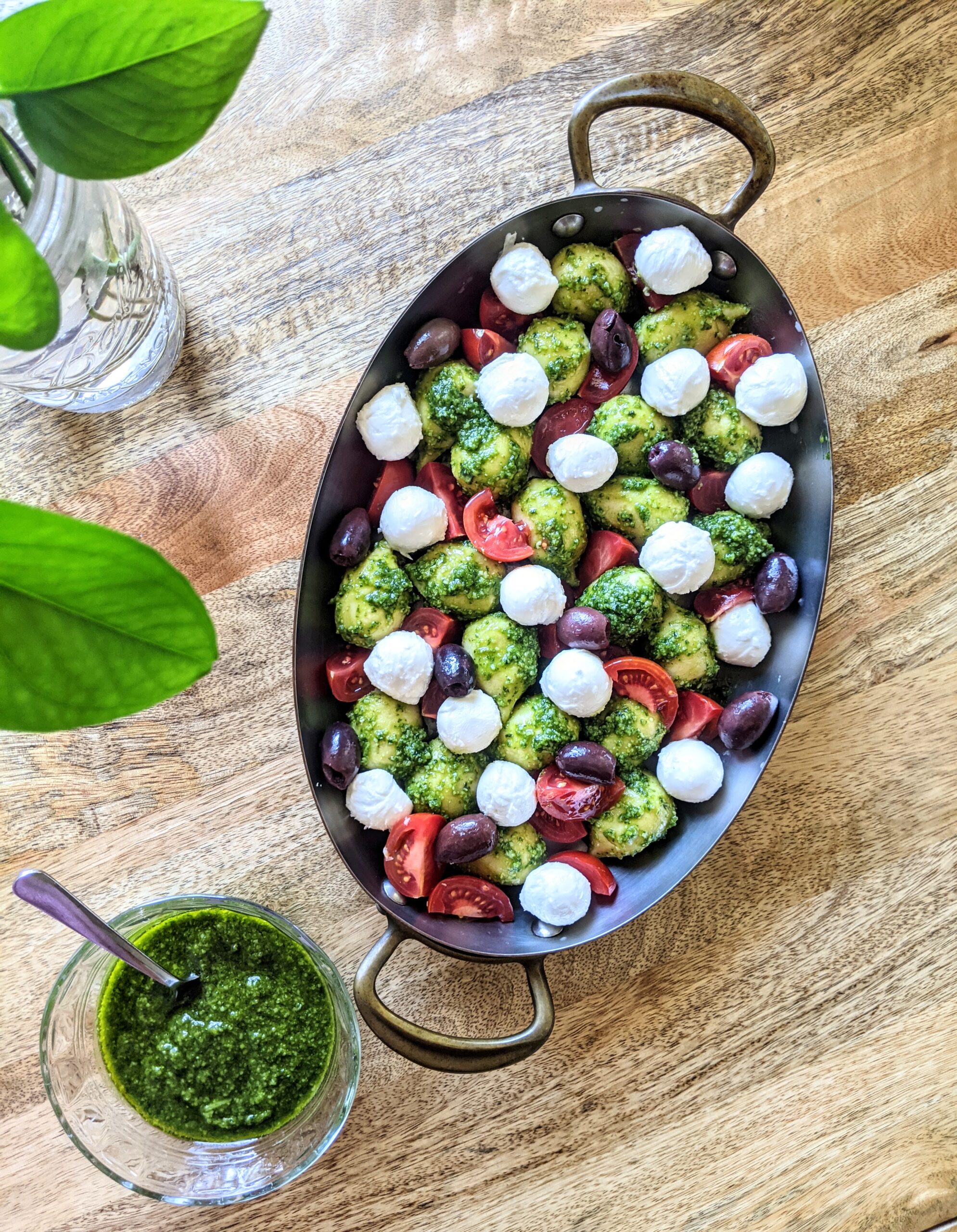 An oval baking dish full of soft gnocchi, small mozzarella balls, tomatoes, Kalamata olives, and fresh basil pesto; ready for the oven!