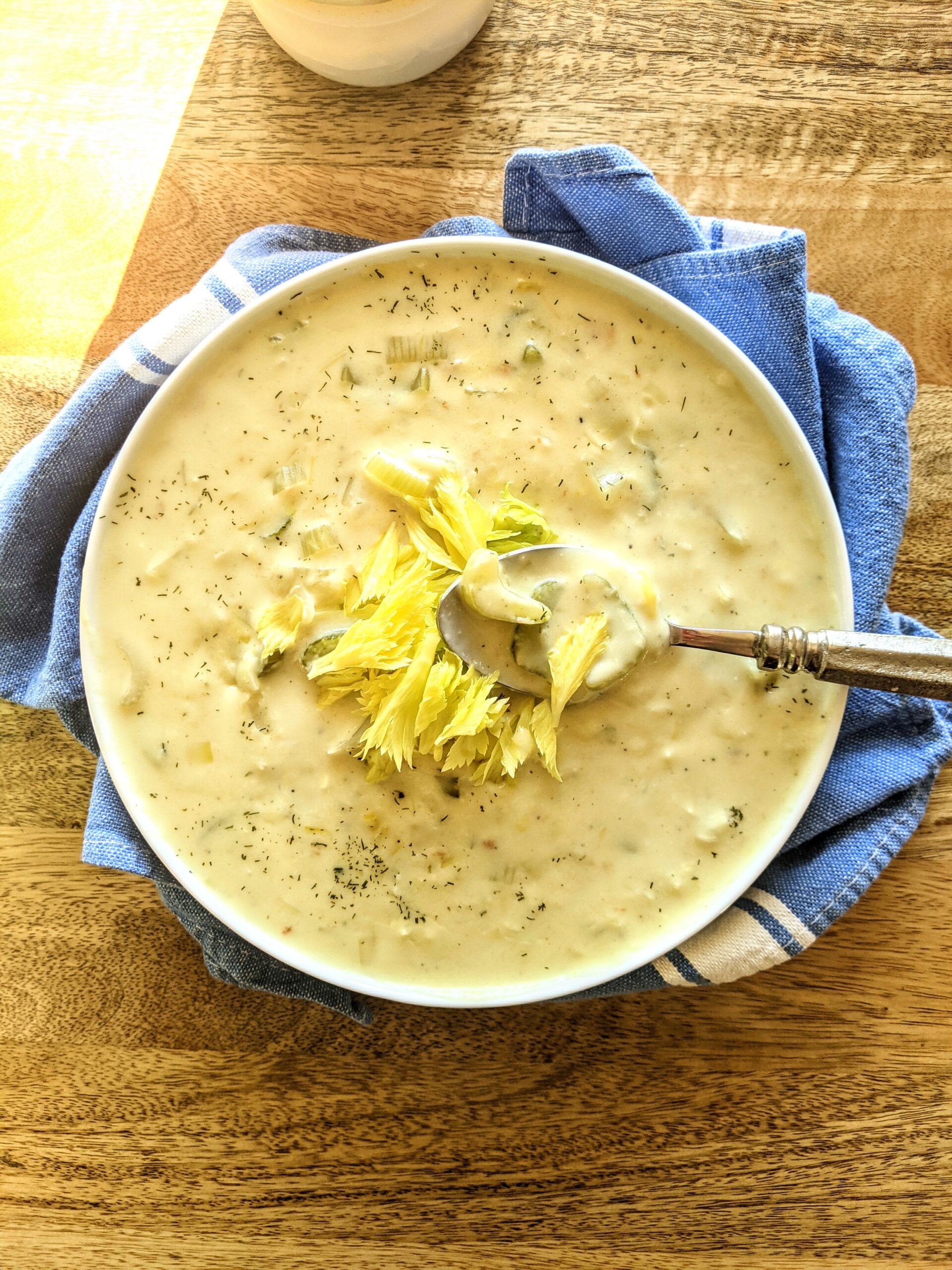 A bowl of comforting Cream of Celery Soup. A large spoonful showcasing pieces of celery, dill, celery leaves, and a thick & creamy chicken broth.