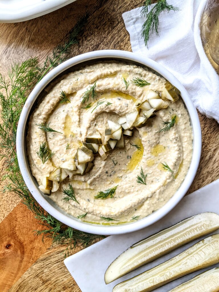 Dill Pickle Hummus garnished with homemade dill pickles, extra-virgin olive oil, and fresh dill.