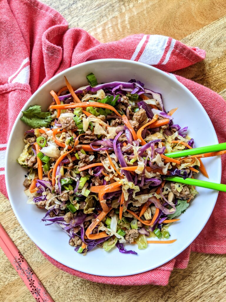 An inside out egg roll in a bowl, no deep frying involved! Shredded purple cabbage, green cabbage, and carrots, tossed with browned ground pork and all the flavors reminiscent of traditional egg rolls.