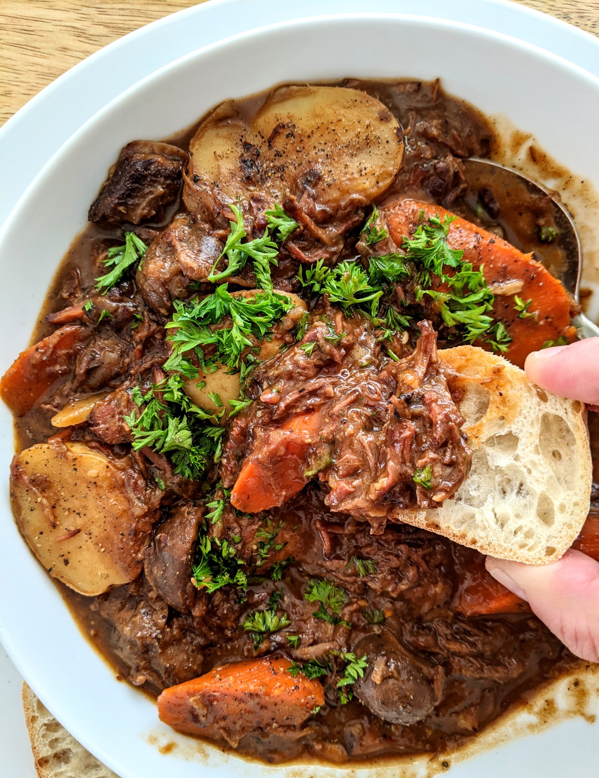 A piece of French bread being dunked into a hearty beef stew; a French classic. Several hours of braising in the oven resulting in tender meat that melts into the stew.