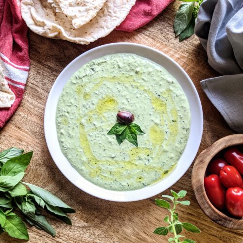 A plate of fresh herb and labneh dip, garnished with a Kalamata olive and a few basil leaves. Serve alongside warm pita bread and San Marzano tomatoes.