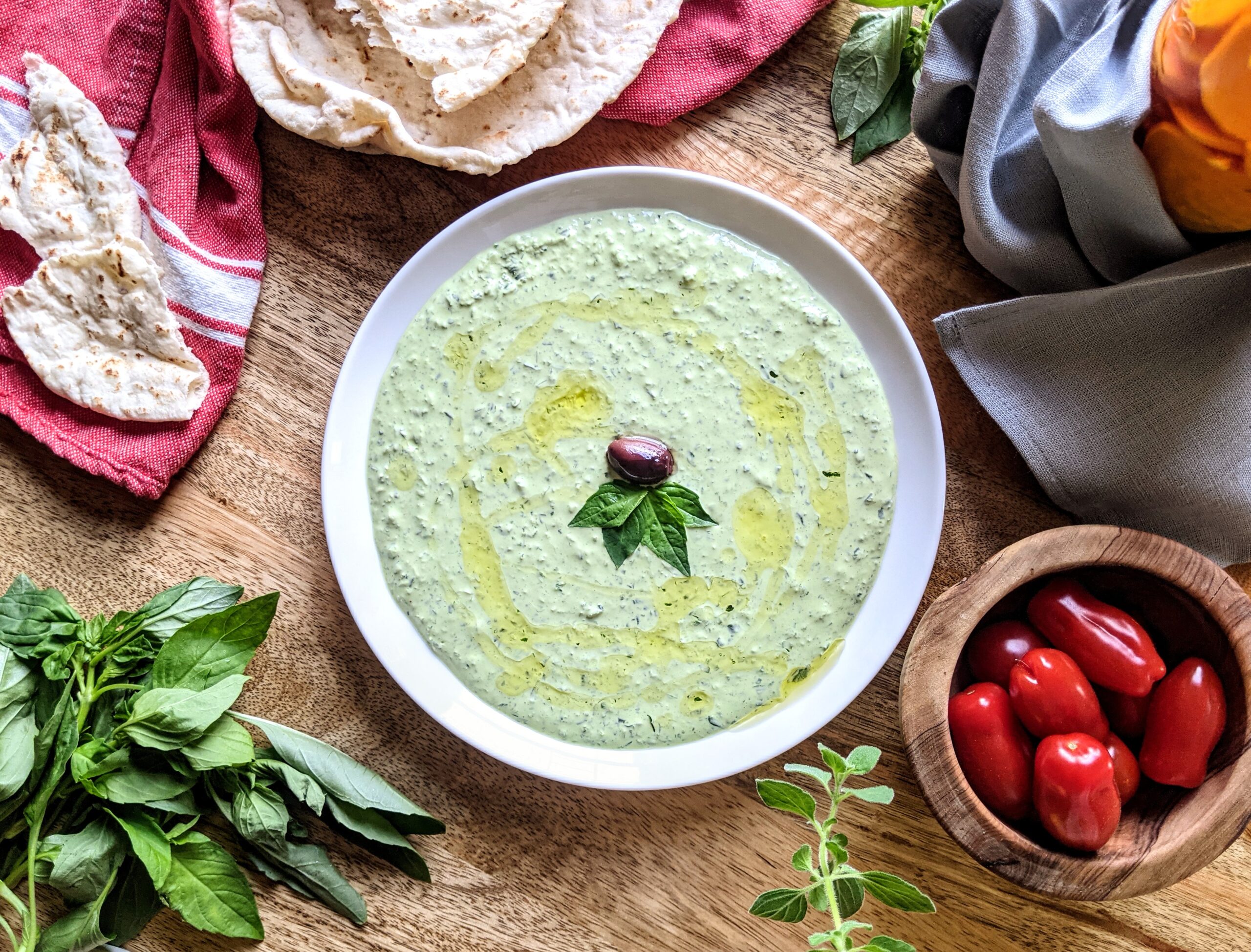 A plate of fresh herb and labneh dip, garnished with a Kalamata olive and a few basil leaves. Serve alongside warm pita bread and San Marzano tomatoes.