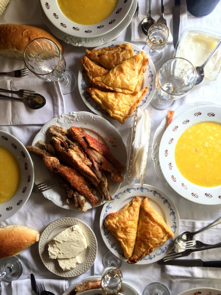 A tablescape of Albanian food. Whole fish, acini di pepe soup, feta, bread, dips.