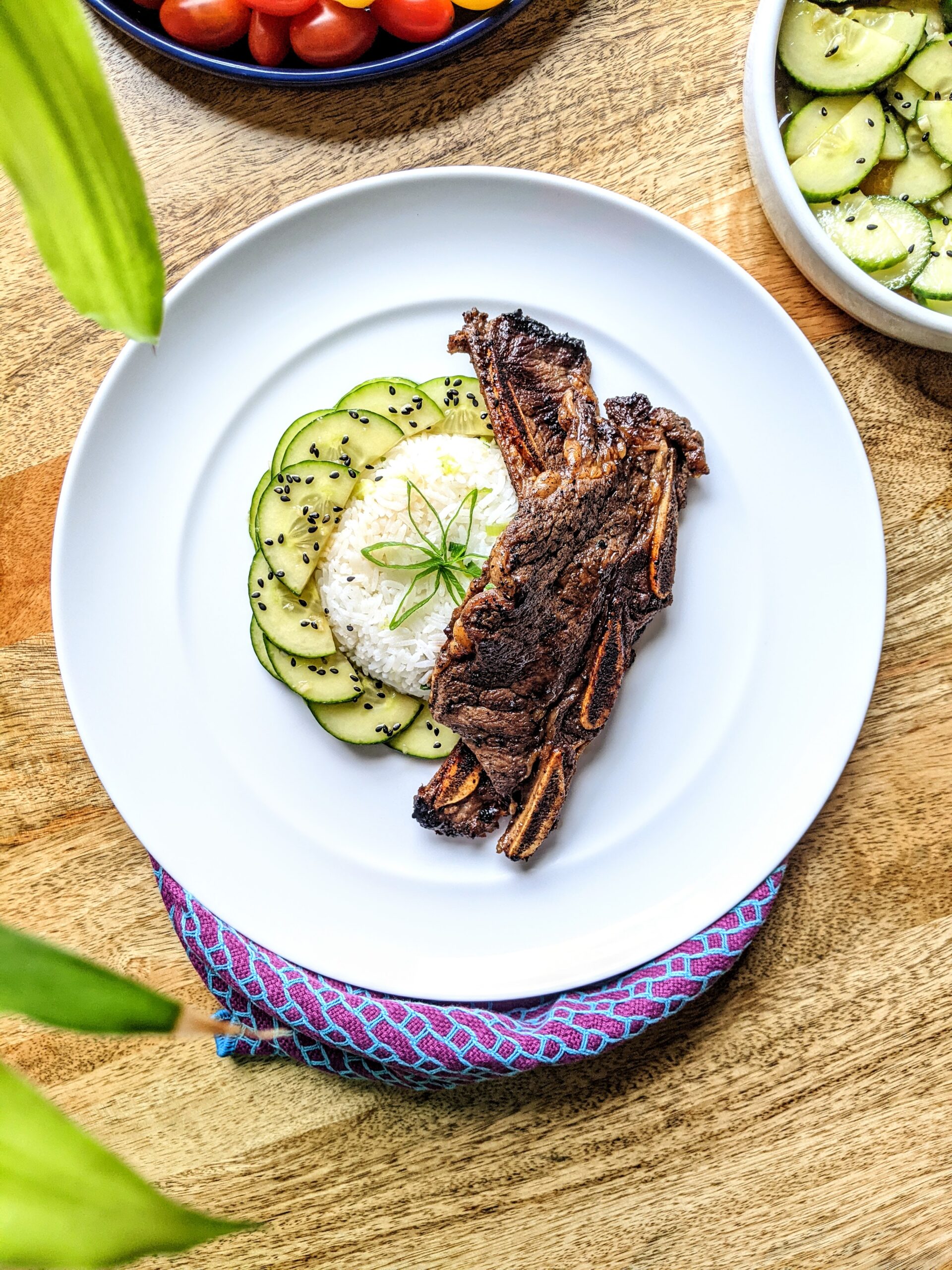 Two grilled Korean BBQ short ribs draped over Jasmine rice and cucumber salad with toasted sesame seeds.