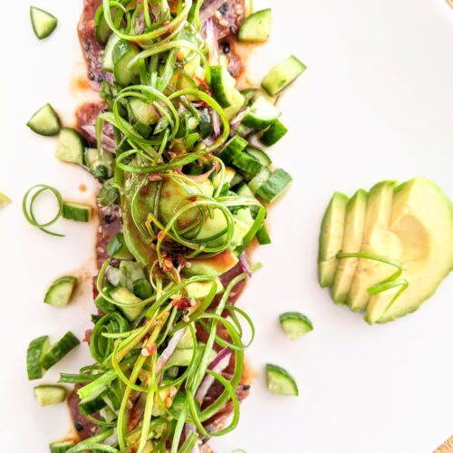Marinated spicy ahi tuna tataki, topped and surrounded by spring onion curls, avocado slices, and diced cucumber salad.