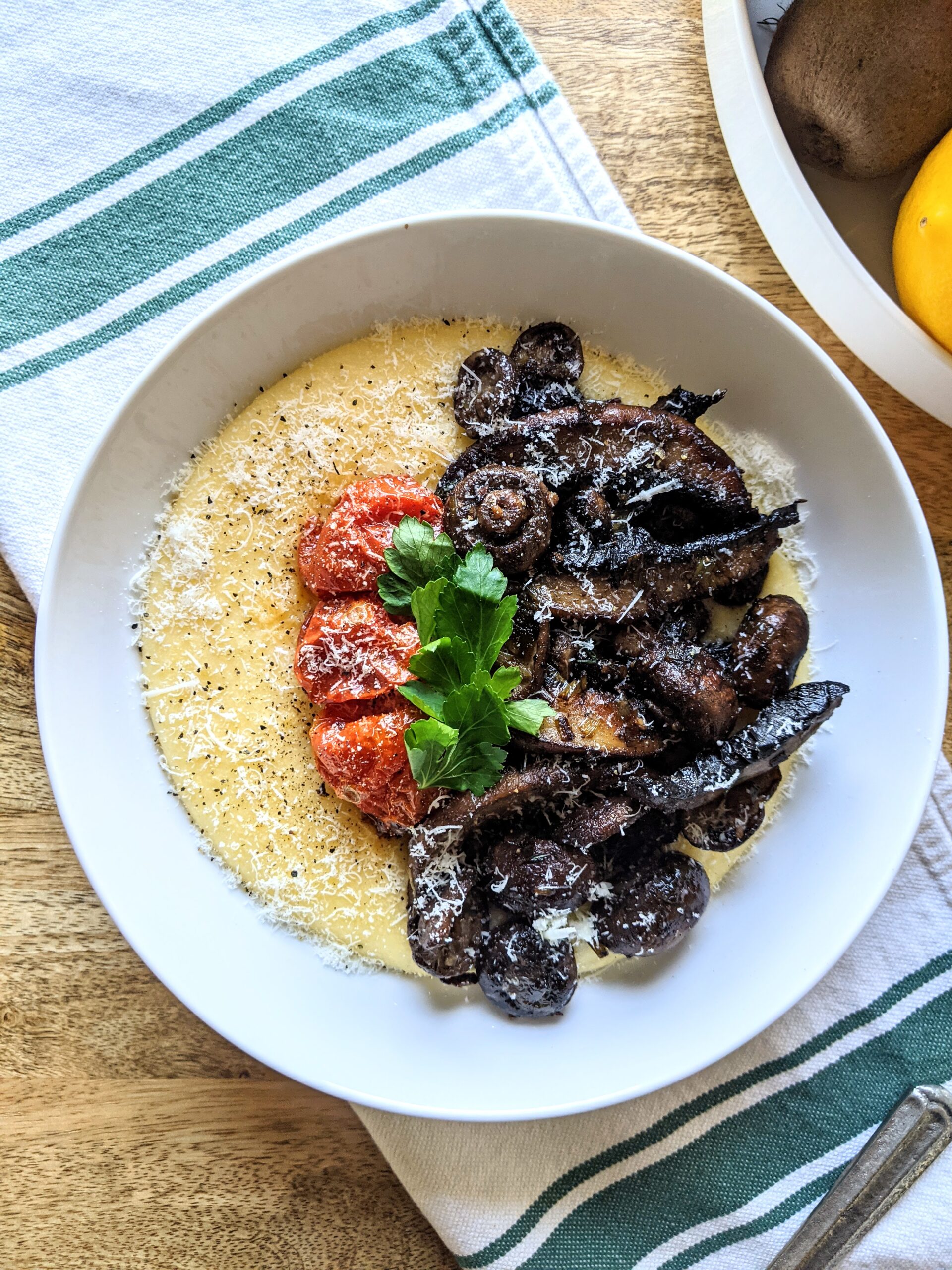 A bowl of creamy Pecorino polenta, topped with assorted mushrooms cooked with cognac and garlic. Garnished with 3 small roasted tomatoes and Italian parsley.