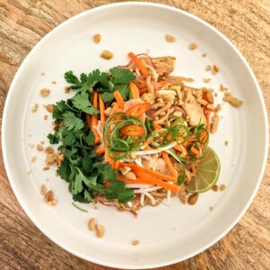 Authentic Pad Thai with rice noodles, shredded vegetables, crushed peanuts, spring onion curls, and fresh cilantro.
