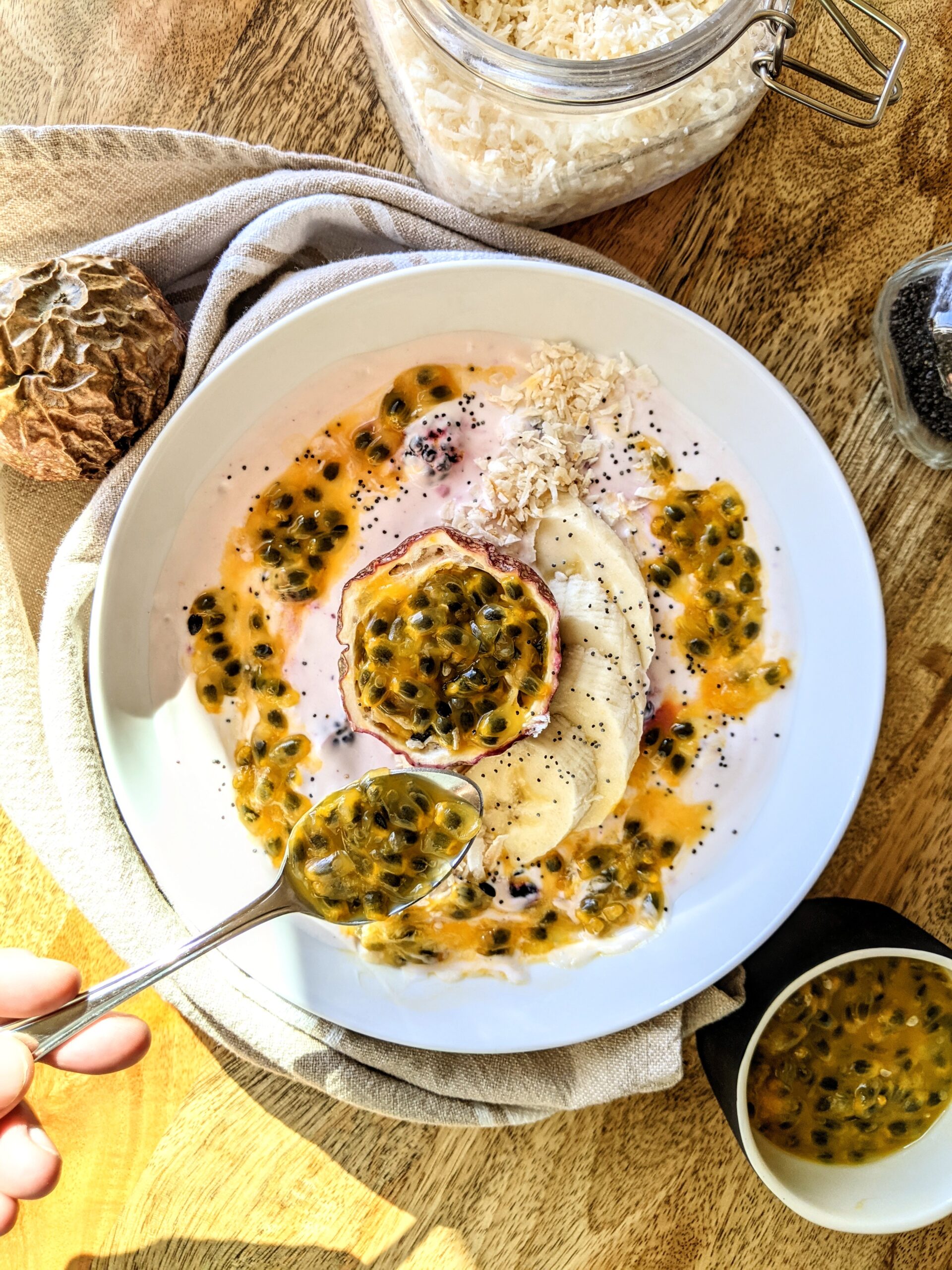 A vibrant breakfast bowl made up of homemade berry yogurt, toasted coconut flakes, sliced banana, chia seeds, and a swirl of ripe passionfruit pulp.