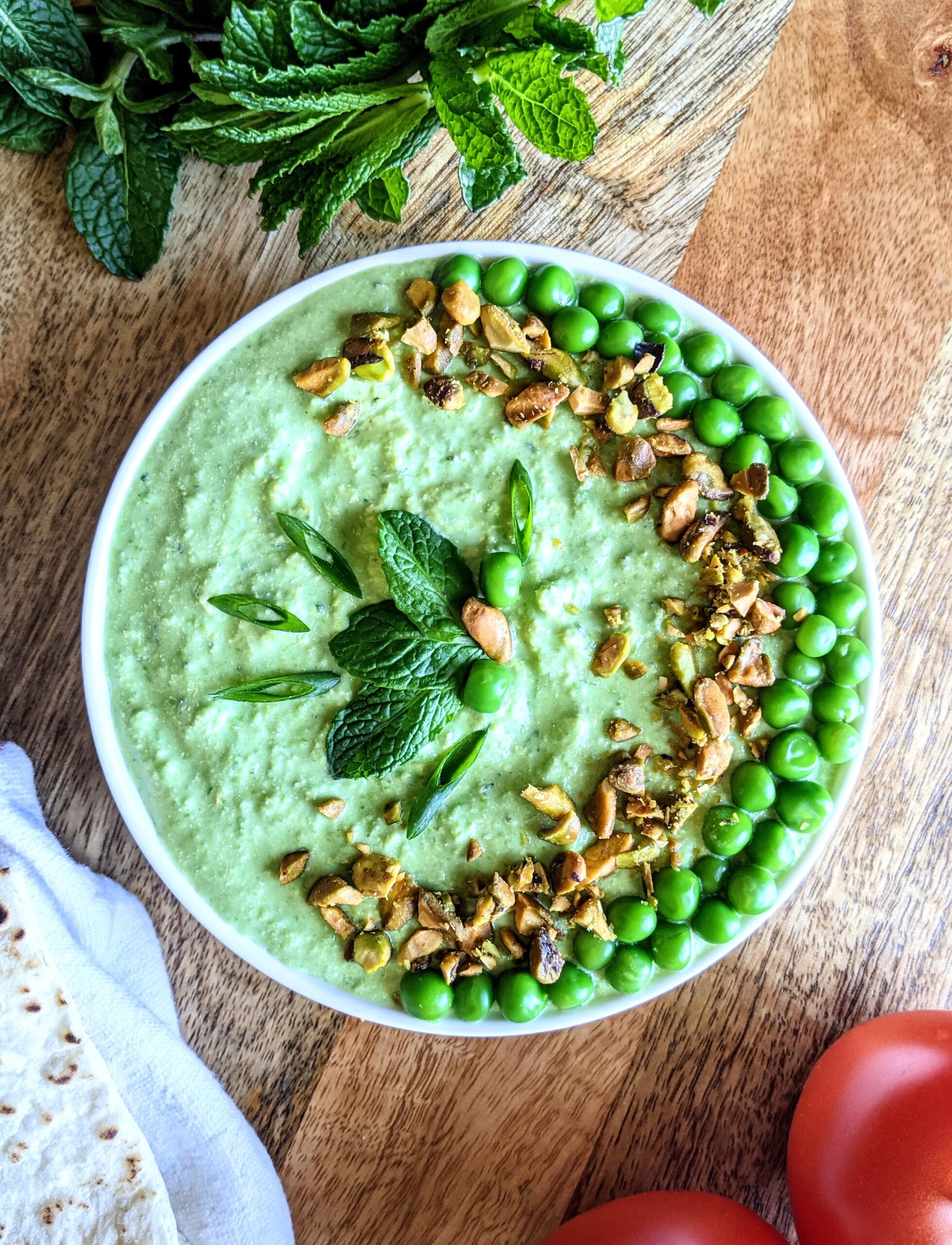A bright green dip make of sweet spring peas and salty feta. Garnished with chopped roasted pistachios and whole steamed peas arranged in the shape of a crescent moon, and a few leaves of fresh mint.