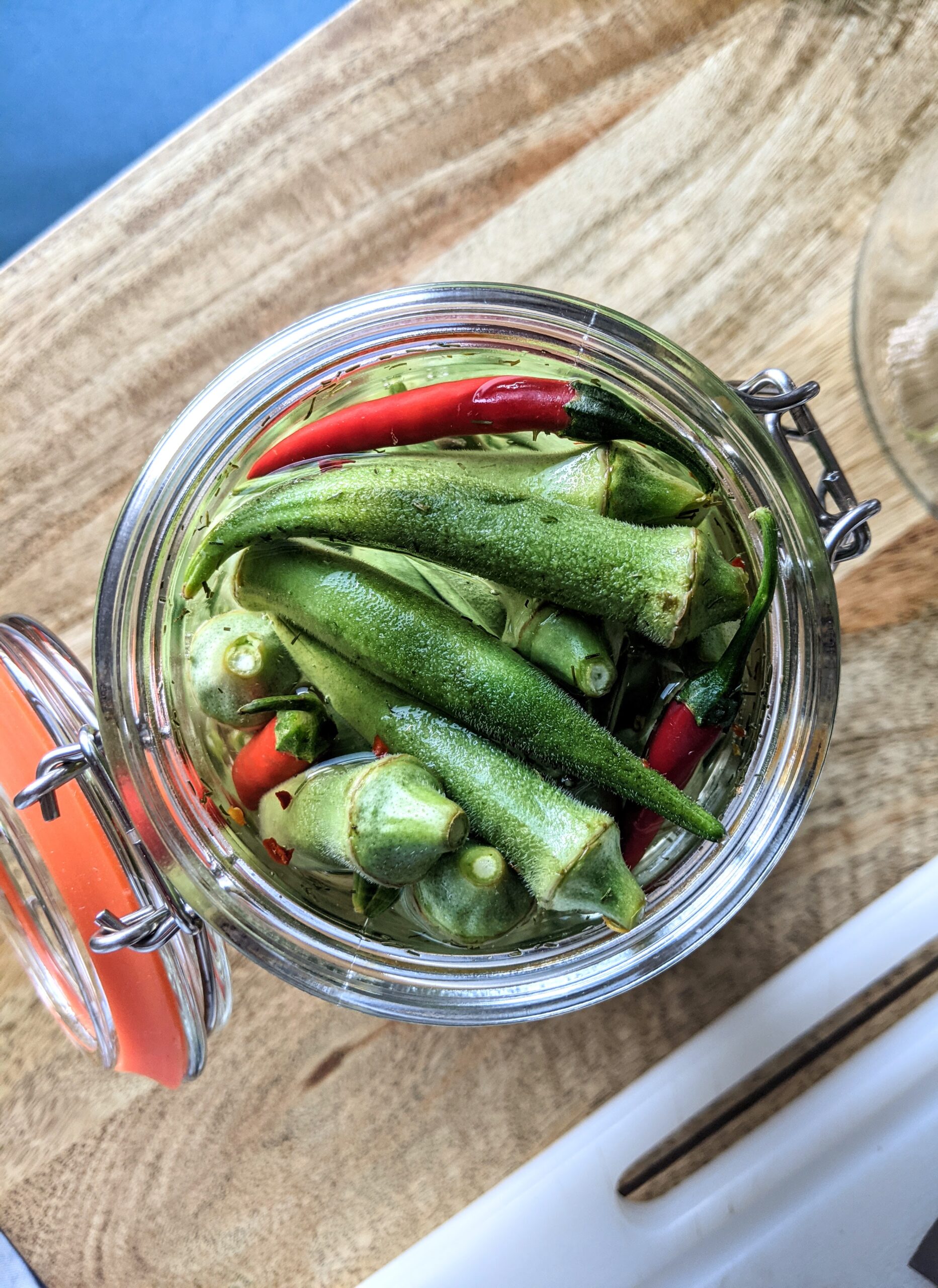 An open jar of pickled okra with garlic, fresh dill, and whole Thai chilies.