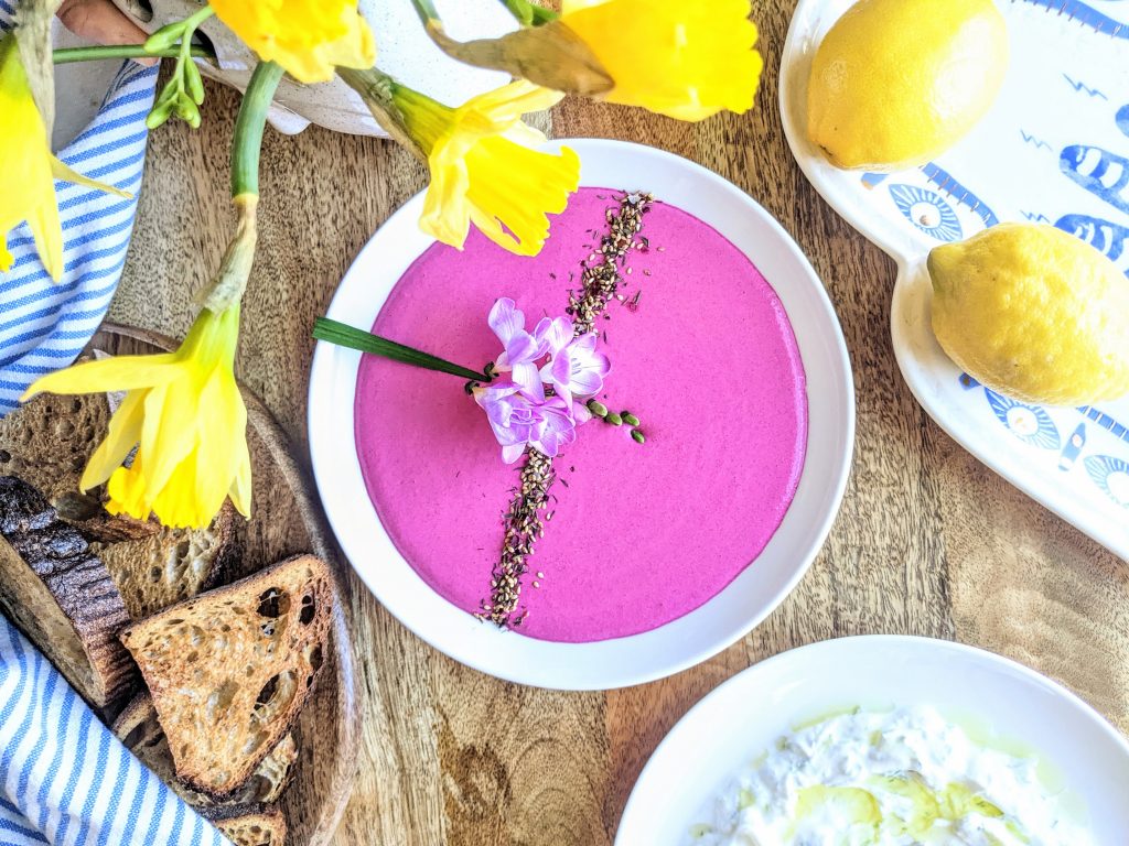 A plate of roasted beet and labneh dip, garnished with za'atar and fresh freesia. Served with sourdough toasts and tzatziki.