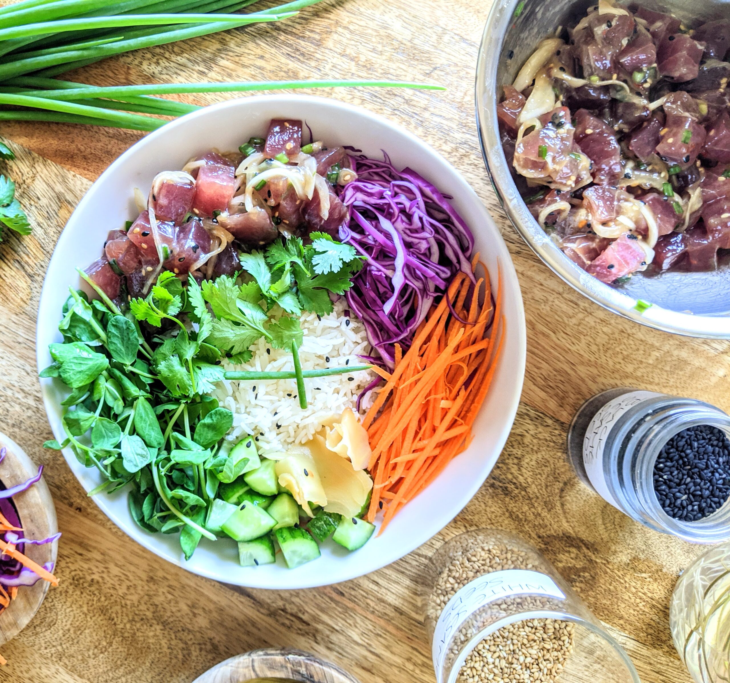 A vibrant and colorful Hawaiian Tuna Poke Bowl, filled with cubes of marinated ahi tuna, shredded purple cabbage and carrots, diced Persian cucumbers, pea shoots, pickled ginger and steamed Jasmine rice. Garnished with sliced Japanese scallion and toasted sesame seeds.
