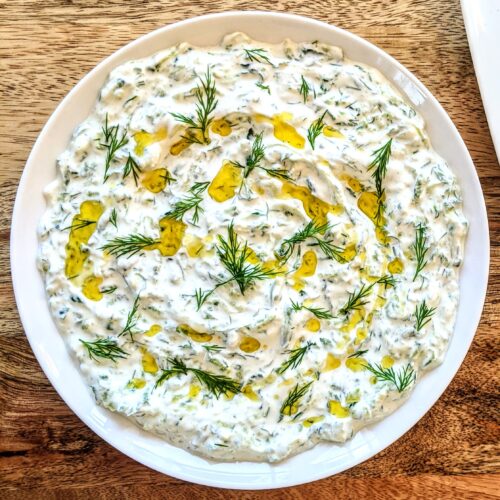 A shallow plate of homemade tzatziki, with a generous drizzle of extra-virgin olive oil; garnished with torn dill.