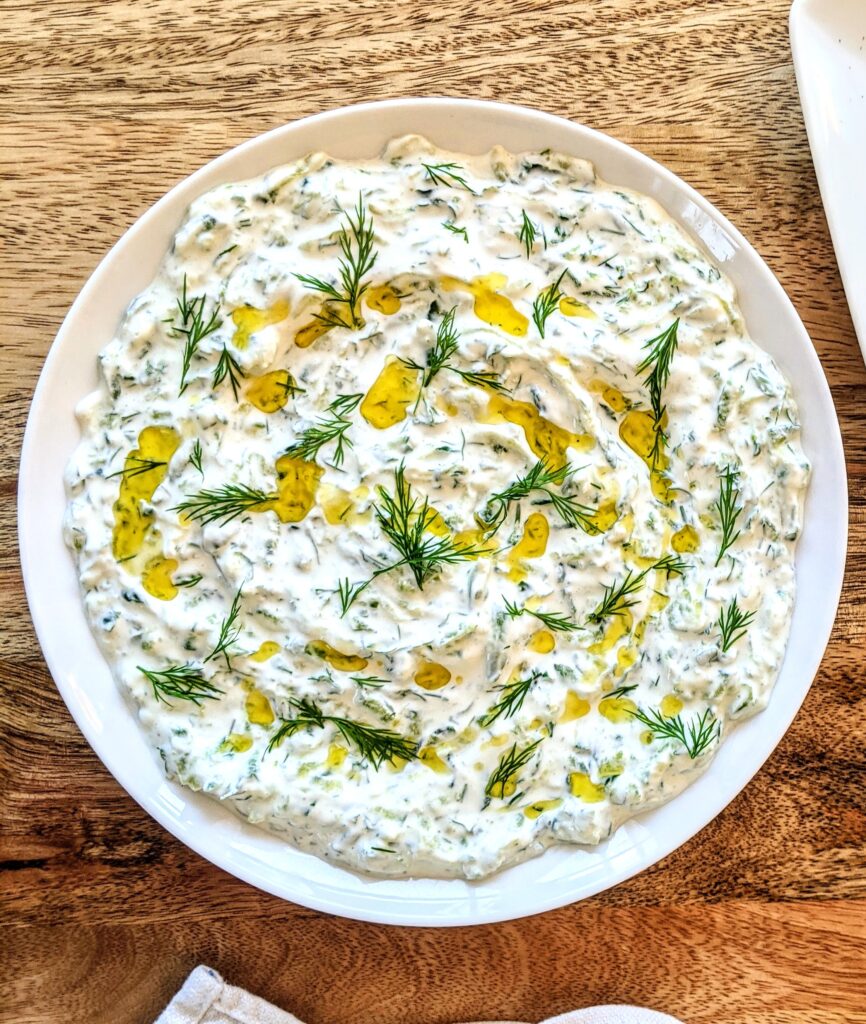 A shallow plate of homemade tzatziki, with a generous drizzle of extra-virgin olive oil; garnished with torn dill.