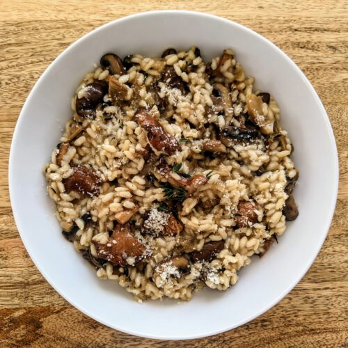 A bowl of earthy and savory wild mushroom risotto topped with finely grated Parmigiano Reggiano. This dish features chanterelles, crimini, and dried porcini mushrooms.