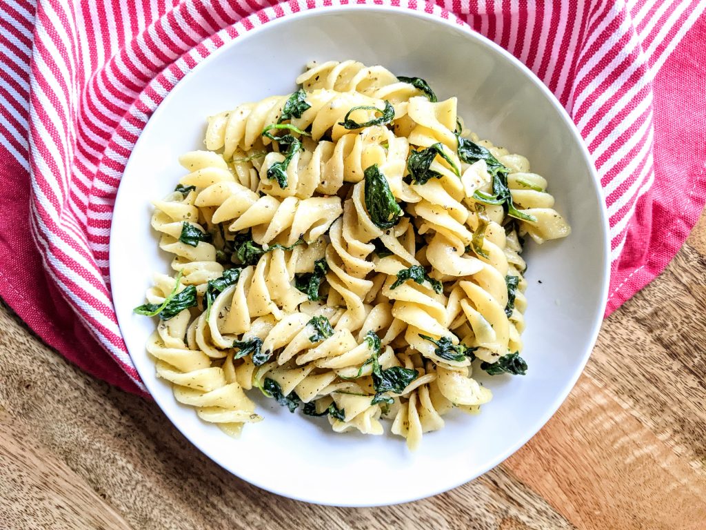 A bowl of Boursin pasta with spinach and a white and red kitchen towel loosely draped.