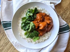 A bowl of butter chicken, served over Jasmine rice, garnished with fresh cilantro.