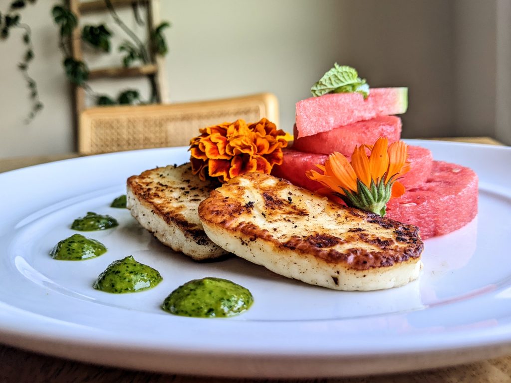 Dots of mint & cilantro pesto, grilled halloumi, watermelon, and edible flowers.