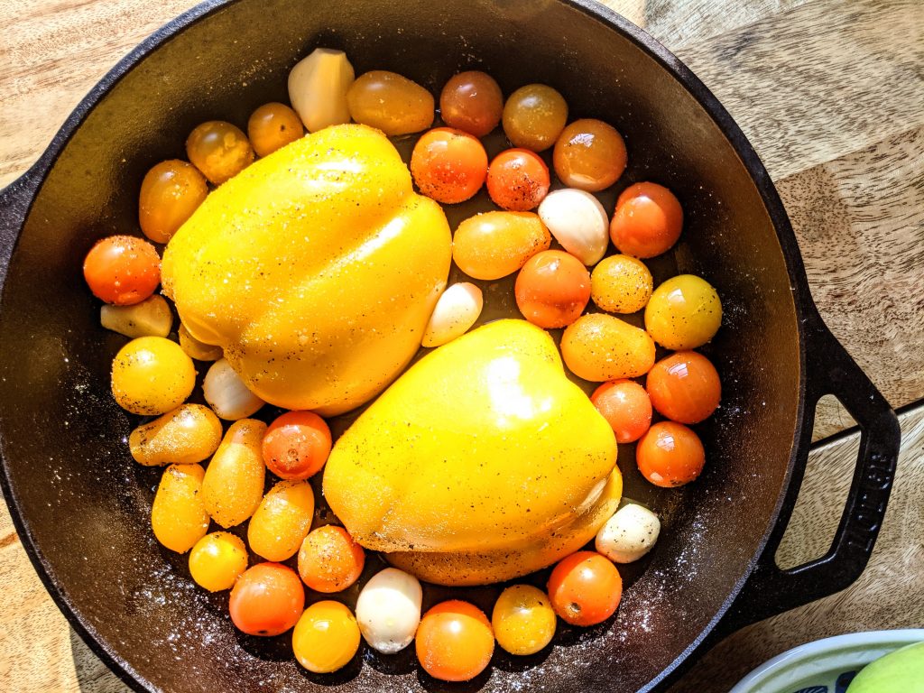 sungold tomatoes, yellow bell pepper, and garlic cloves ready to be roasted in a cast iron skillet.