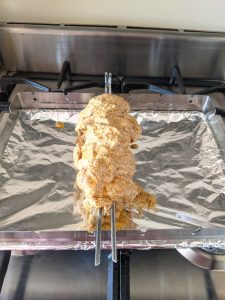 Marinated chicken thighs skewered and suspended on a rack or lasagne pan.