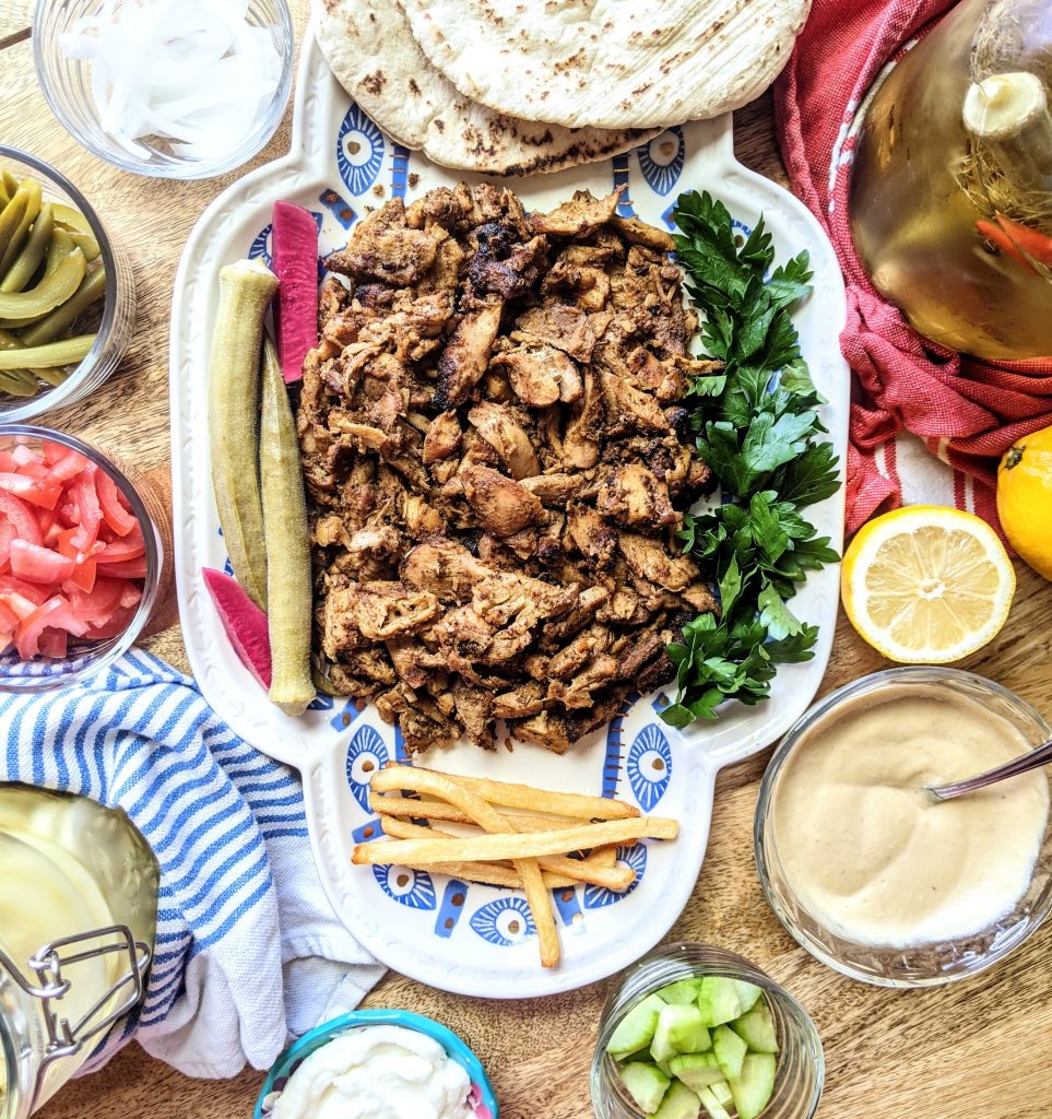 A build your own chicken shawarma platter with pickles, tomatoes, cucumbers, French fries, Toum, and lemon & tahini sauce.