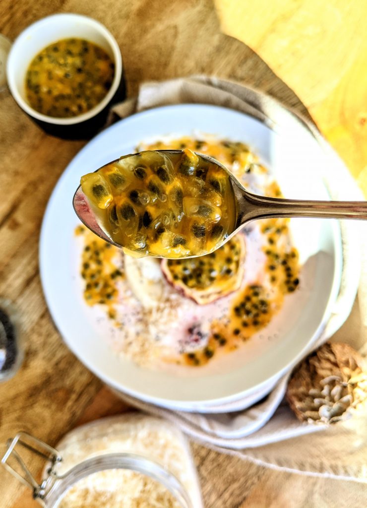 A spoonful of passionfruit pulp overtop a yogurt and fruit breakfast bowl.
