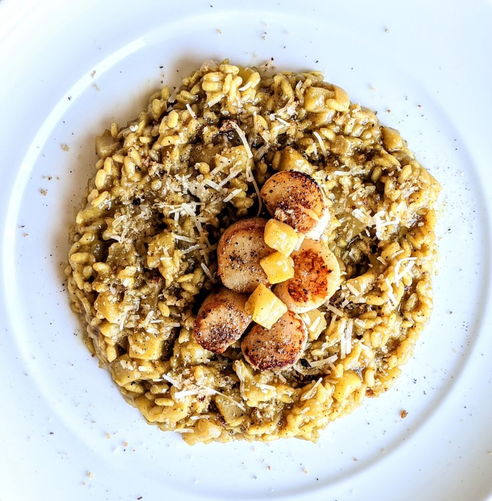 An aerial close up of Curried Apple Risotto with five seared scallops and a few pieces of diced apple.