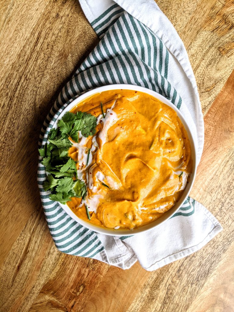 A bowl of vibrant orange Carrot Coconut Curry Soup, garnished with coconut cream and fresh cilantro. 