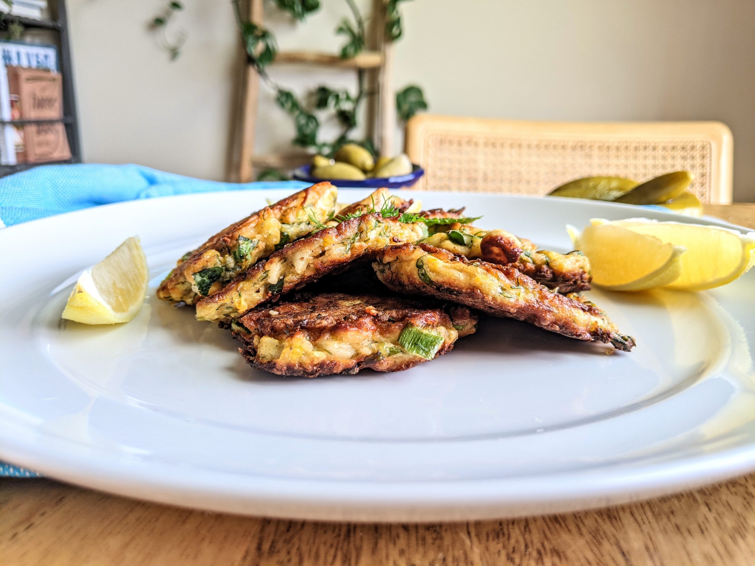 A sideview of 4 Zucchini and Feta Fritters with lemon wedges.