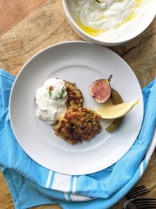 Two Zucchini and Feta Fritters with a dollop of yogurt sauce on top. Serve with a lemon wedge, Mission figs, and Turkish pickles.