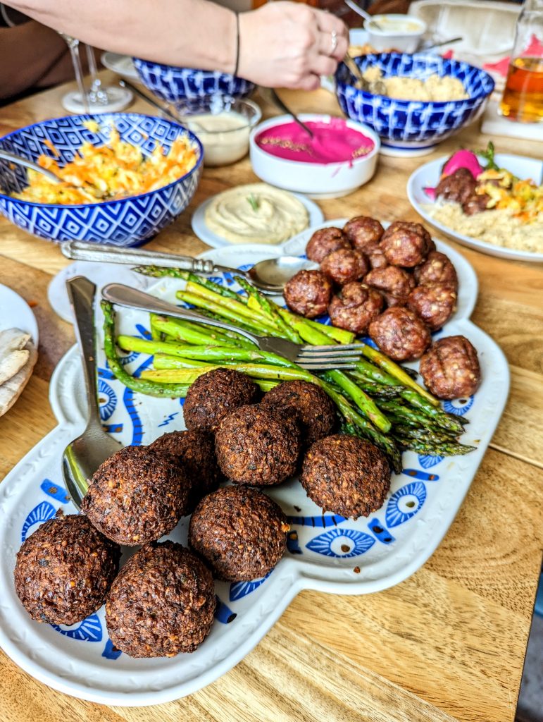 A long platter of falafels, roasted asparagus, and baked meat. Serve alongside a variety of dips and salads.