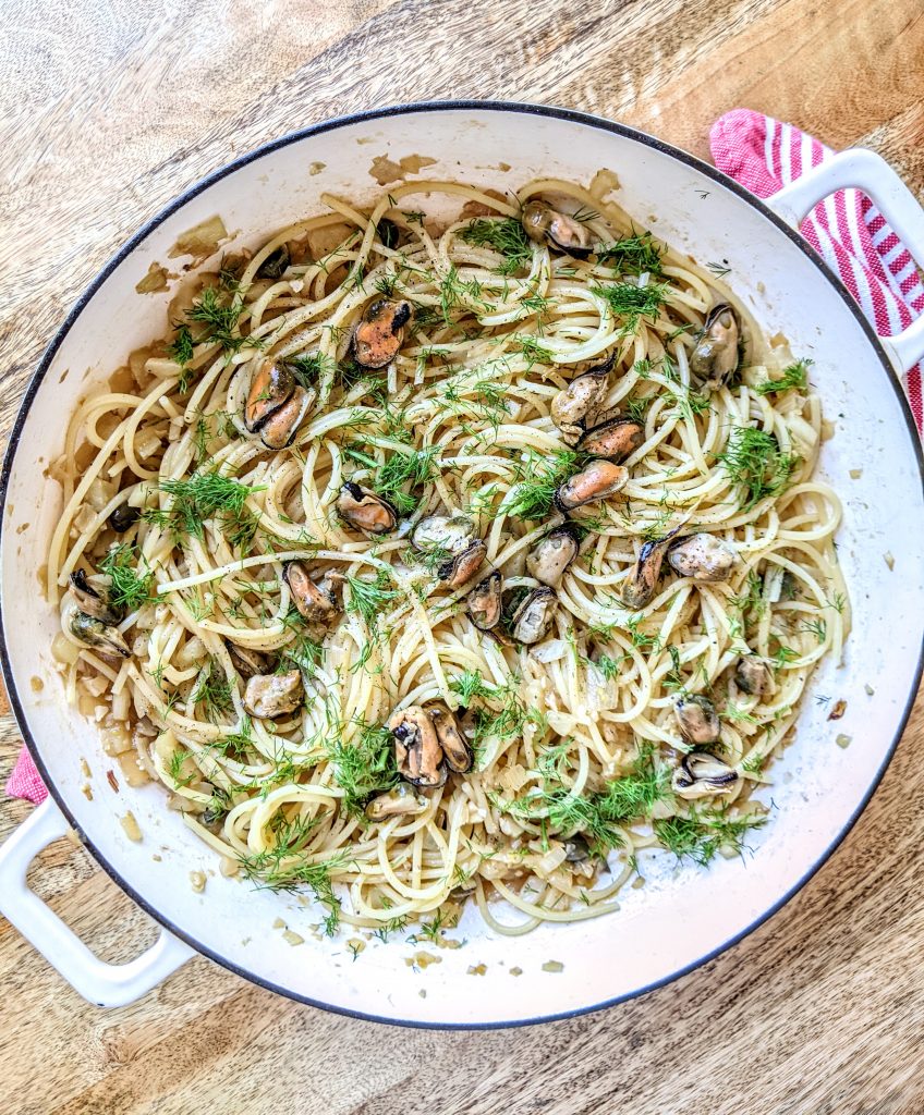 A white skillet full of smoked mussel spaghetti with fennel fronds as garnish.