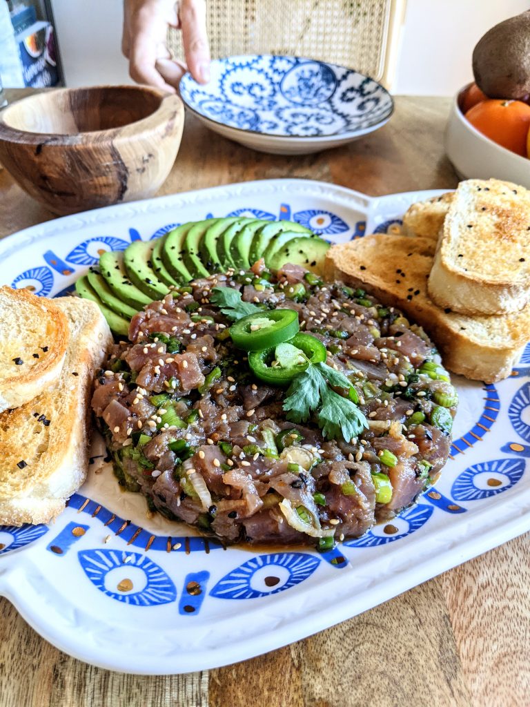 A platter of Tuna Tartare, ripe avocado slices, and fermented garlic chili toasts.