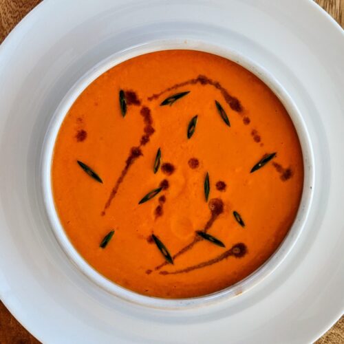A small bowl of vibrant orange Andalusian Gazpacho; garnished with sliced chives and a drizzle of sherry vinegar.