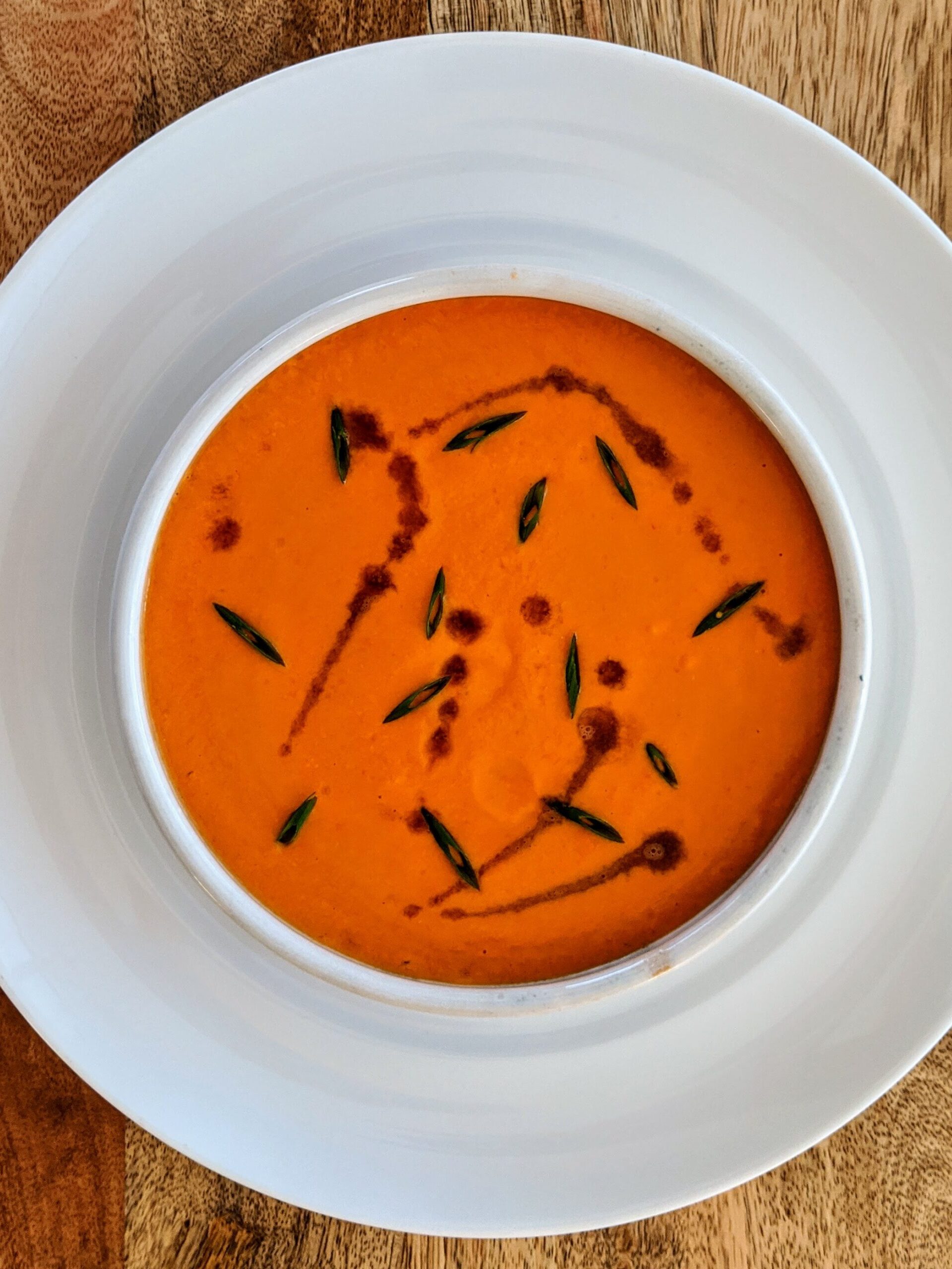 A small bowl of vibrant orange Andalusian Gazpacho; garnished with sliced chives and a drizzle of sherry vinegar.