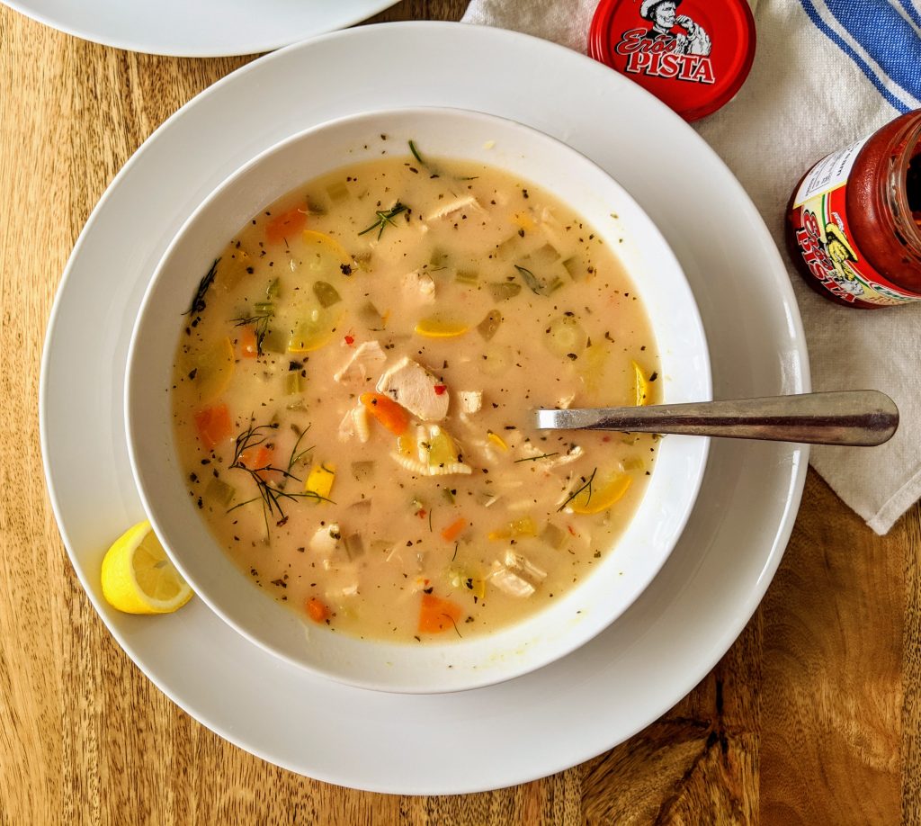 A bowl of Mediterranean chicken and vegetable soup with some chili paste stirred in. You can see pieces of chicken, carrot, zucchini, and celery.