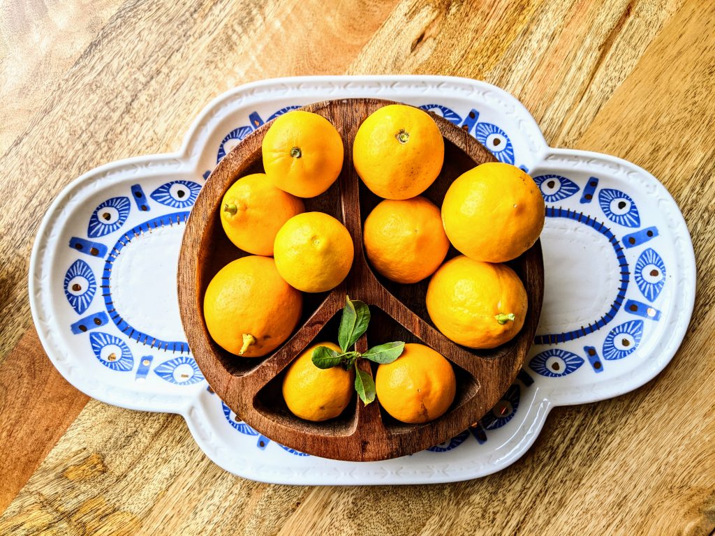 A variety of lemons in a wooden bowl on a serving platter with blue evil eyes.