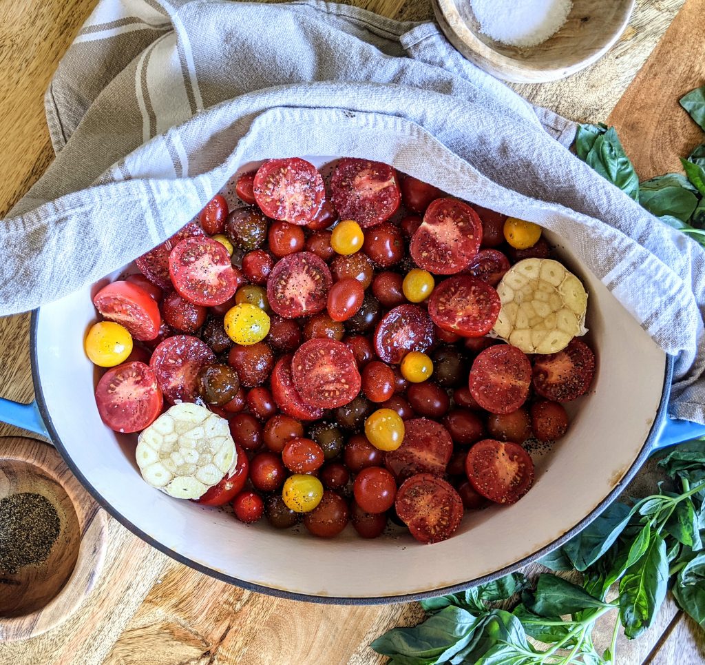 A Dutch oven full of assorted multi-colored tomatoes and garlic ready to roast.