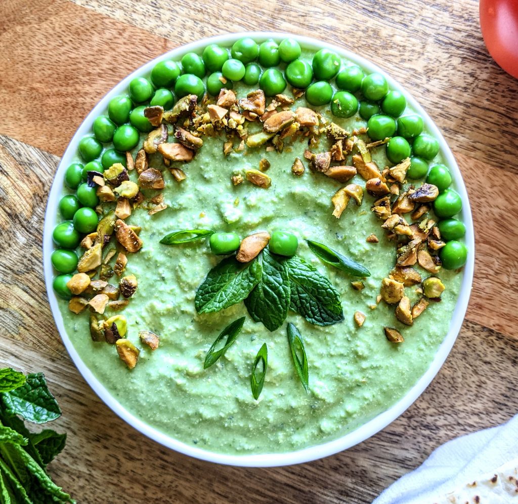 A bowl of Spring Pea with Feta Dip with Mint, topped with whole peas, crushed pistachios, sliced scallions, and mint leaves.