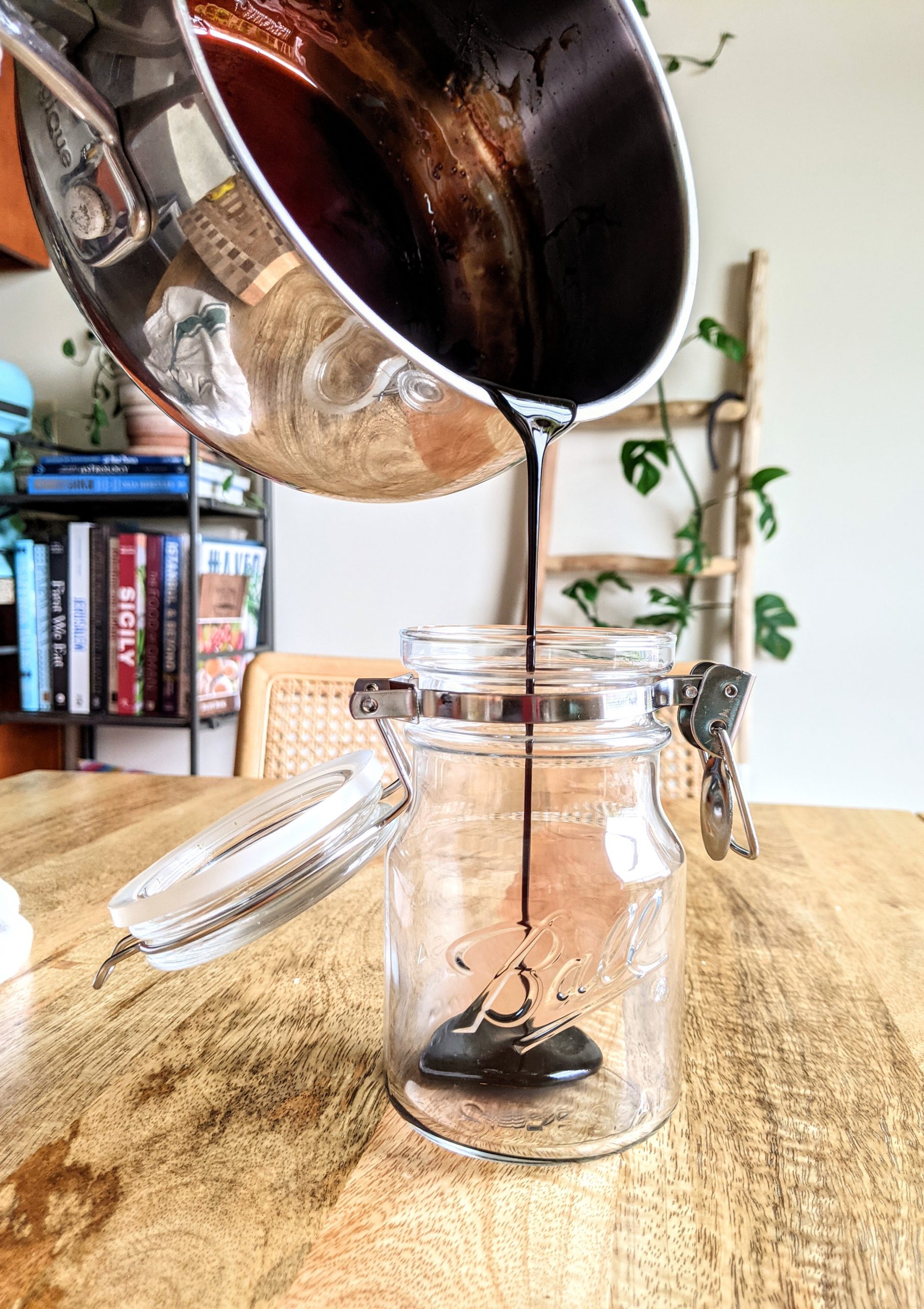 Pouring balsamic glaze from a pot into a jar.