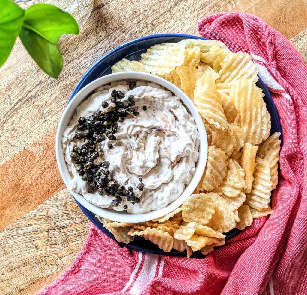 A bowl of Buttermilk French Onion Dip with Fried Capers. Served with thick ridged plain potato chips.