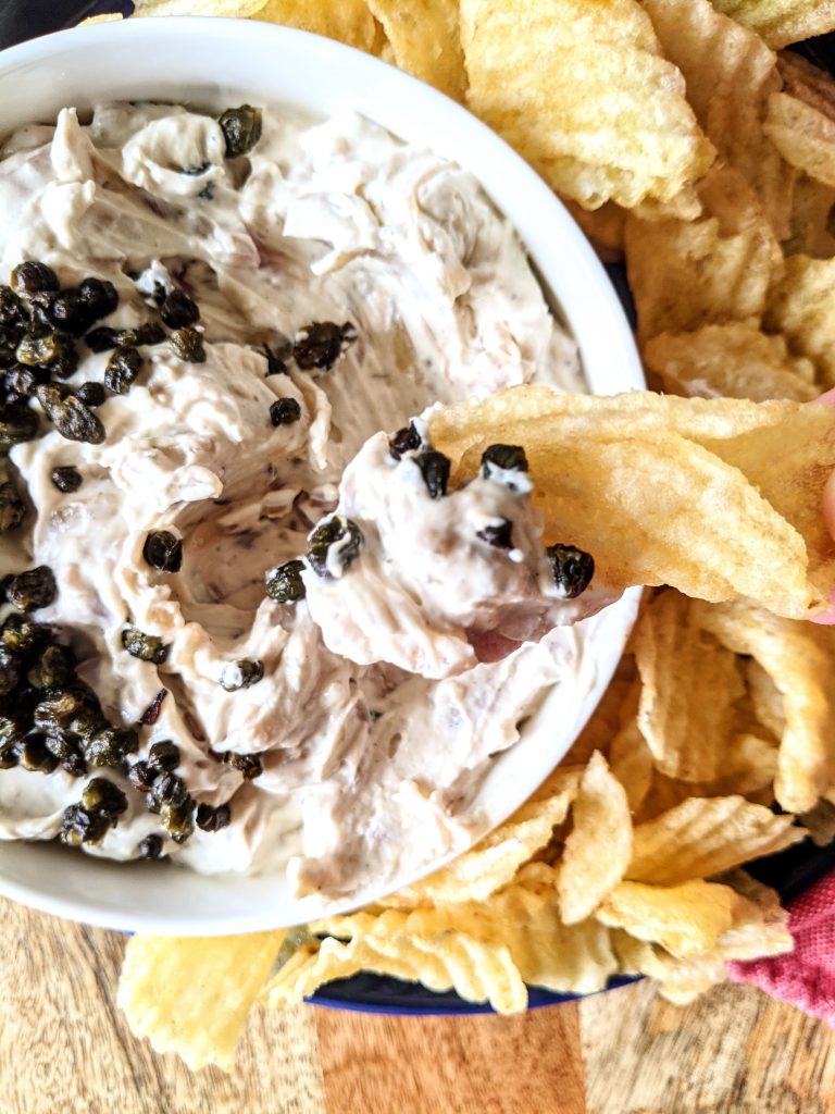 A thick rippled chip dipping into a Buttermilk French Onion Dip with Fried Capers.