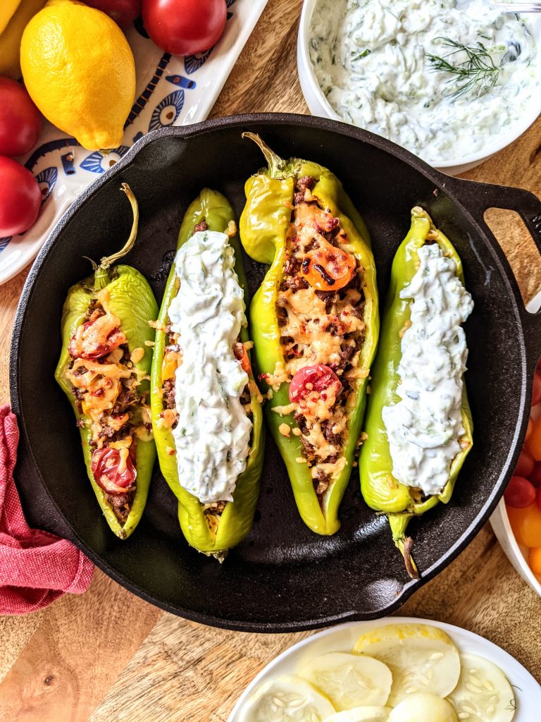 Four Georgian inspired stuffed hatch chili peppers in a cast iron frying pan. Two of the peppers have a tzatziki sauce overtop.